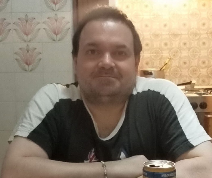 Un uomo con una cartolina di Pistoia, circondato da foto e documenti storici, in una stanza con librerie e computer